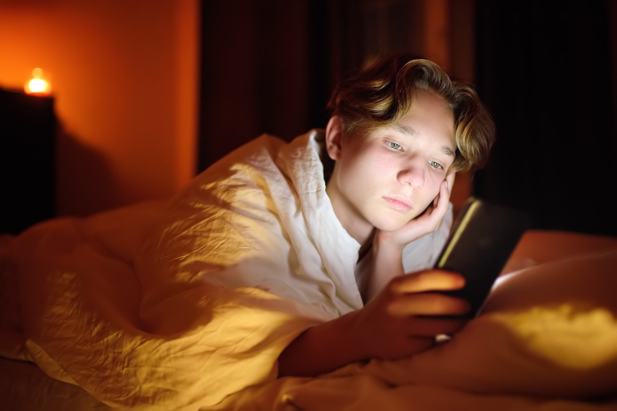 Teenager boy chatting by phone, writing in blog or reading social networks instead sleeping.