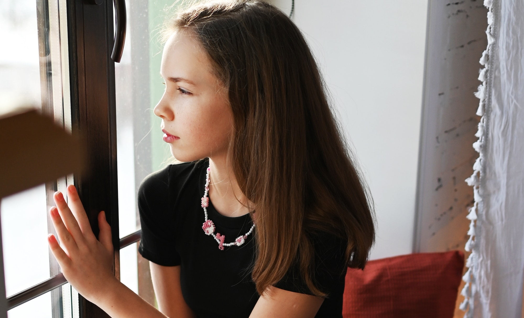 the girl at home looks sadly out of the window. transitional age. emotions